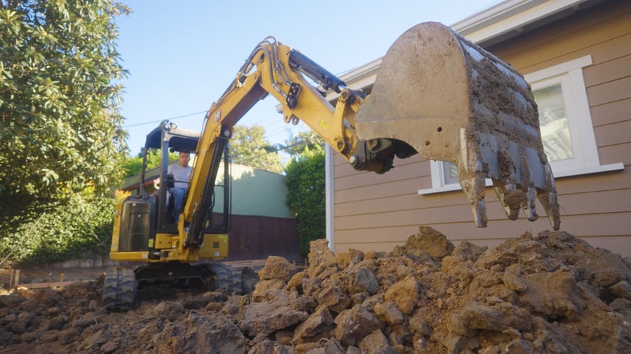 Excavator digging and clearing soil next to the house during construction